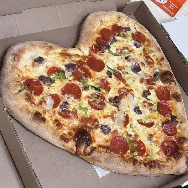 Heart-shaped CraveN Pizza with pepperoni, sausage, green peppers, and onions in a box.