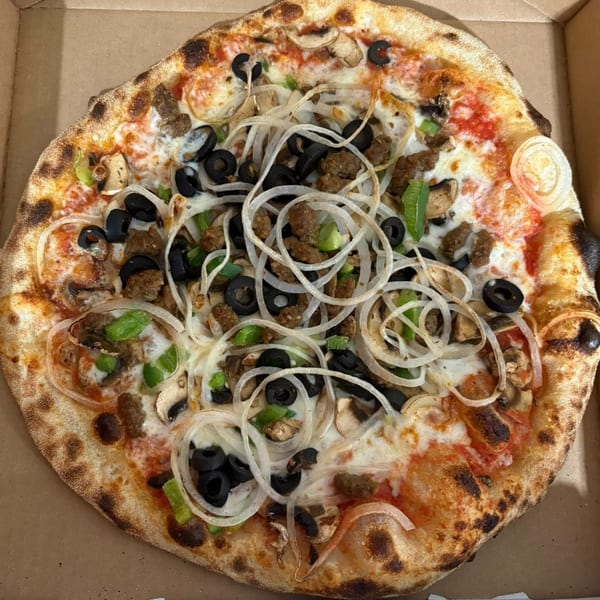 A CraveN Pizza with sausage, mushrooms, black olives, green peppers, and onions in a box.